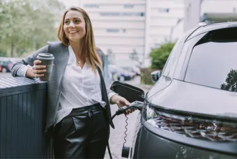 Une jeune fille recharge une voiture électrique avec du café dans l'autre main